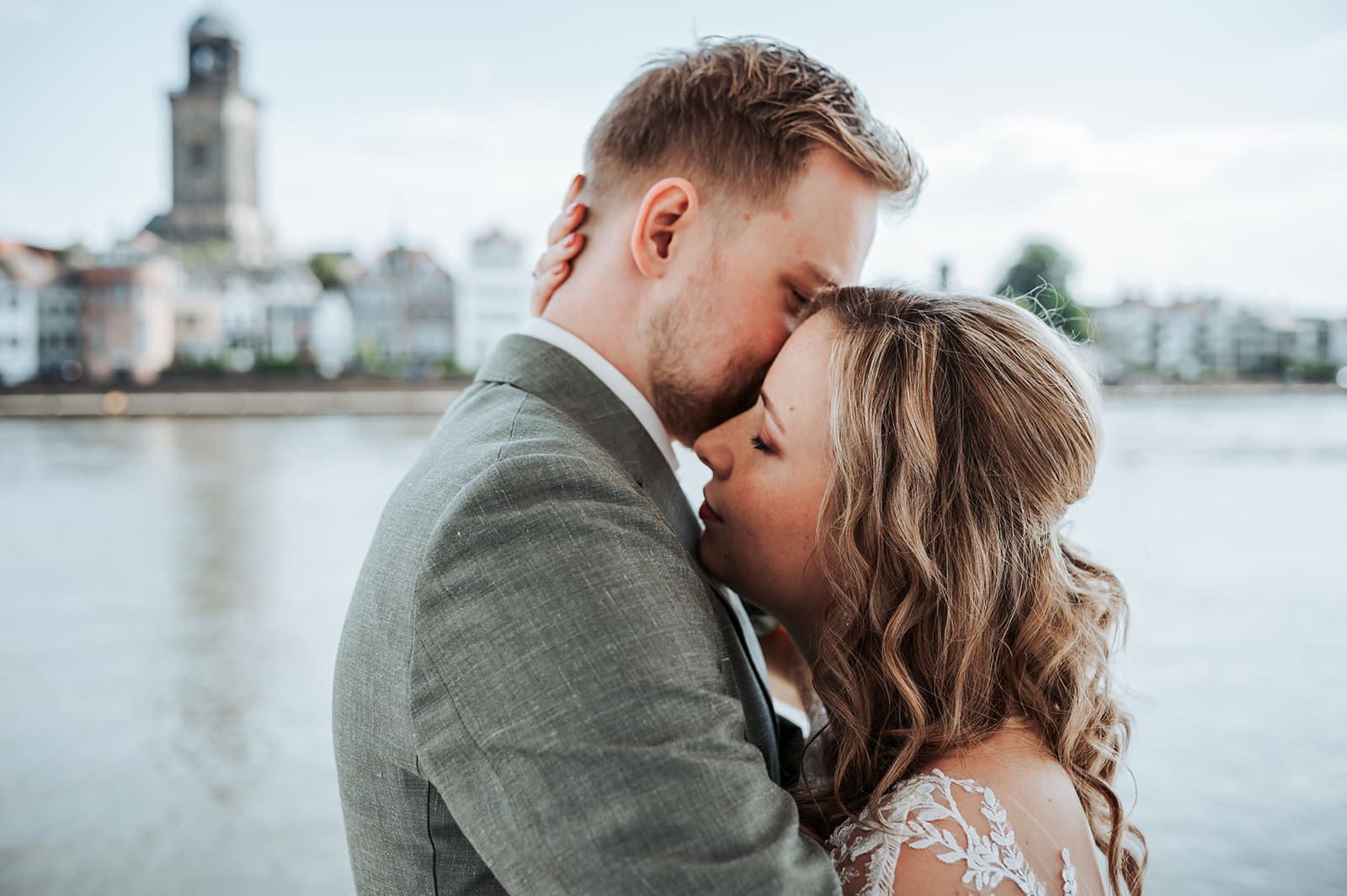 Bruidspaar tijdens de first look aan de IJssel met de skyline van Deventer op de achtergrond