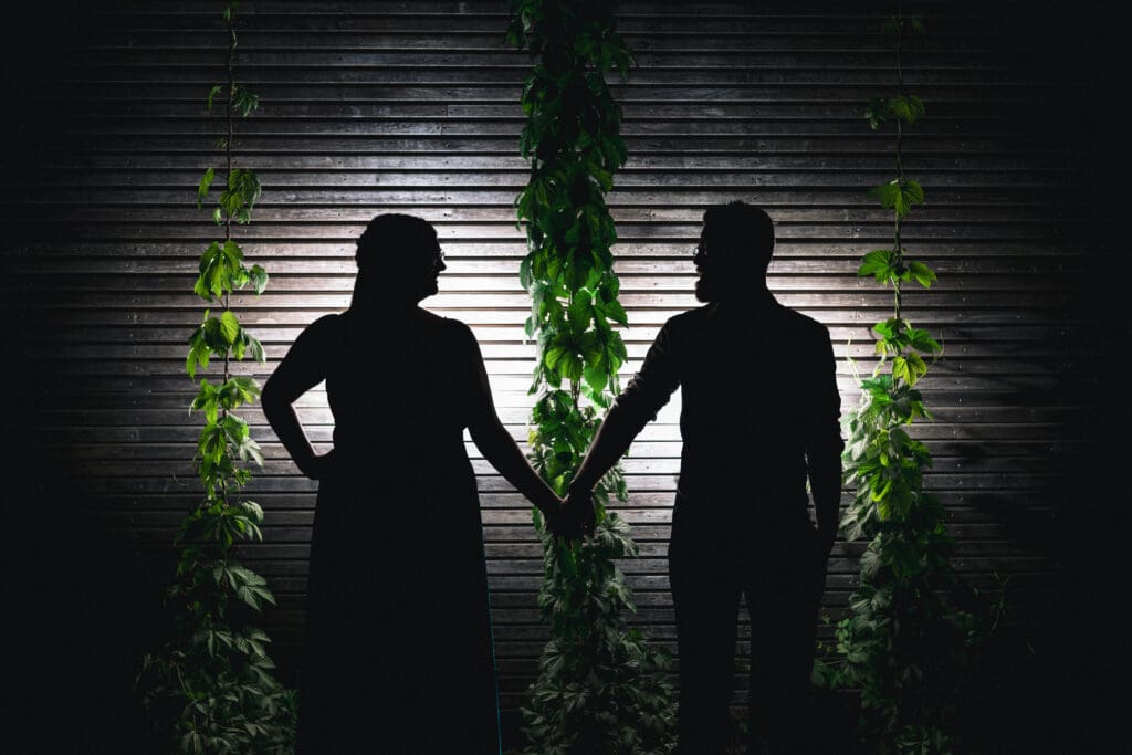 Silhouet van een bruidspaar dat elkaars hand vasthoudt tijdens een avondmoment op hun trouwdag