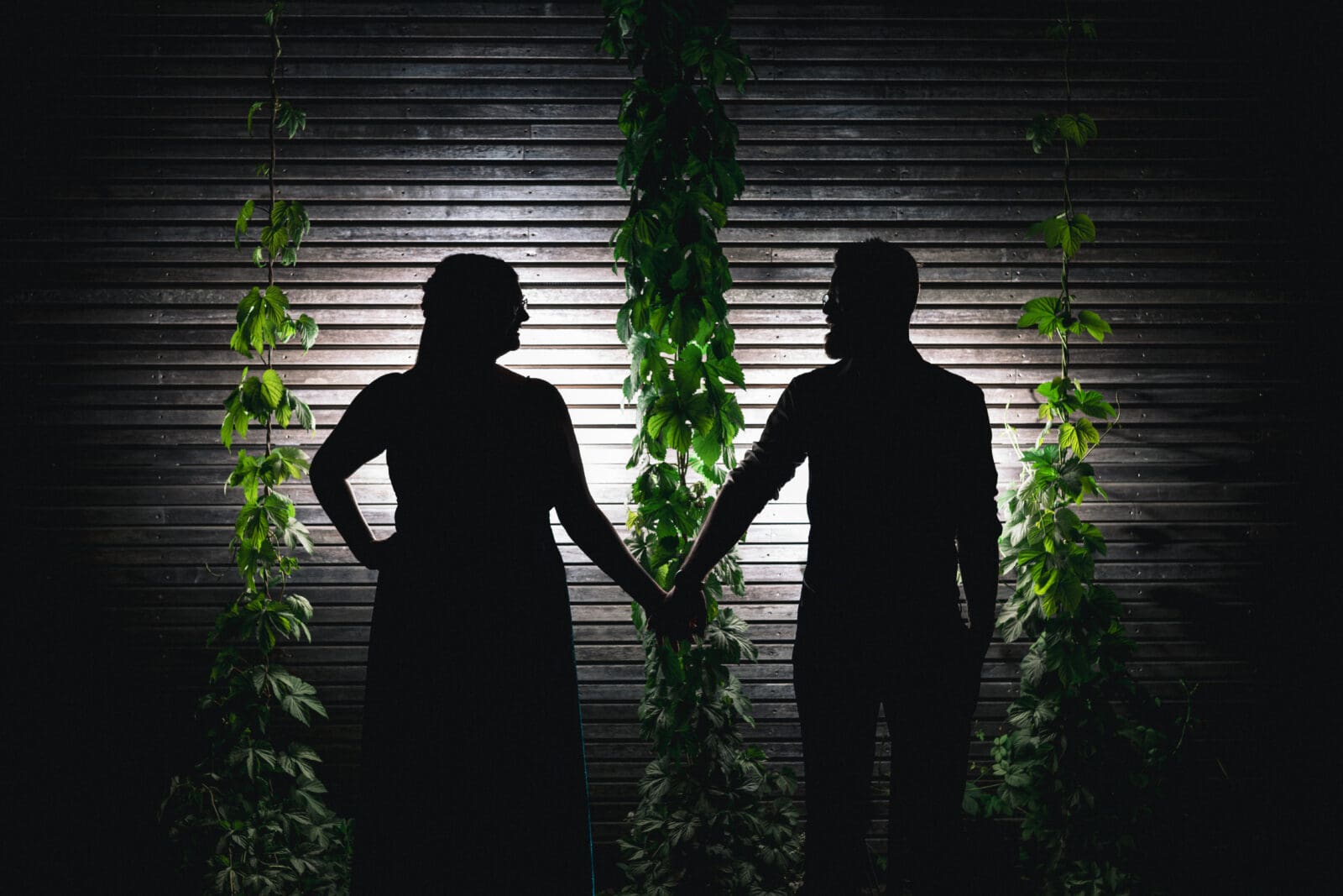 Silhouet van een bruidspaar dat elkaars hand vasthoudt tijdens een avondmoment op hun trouwdag